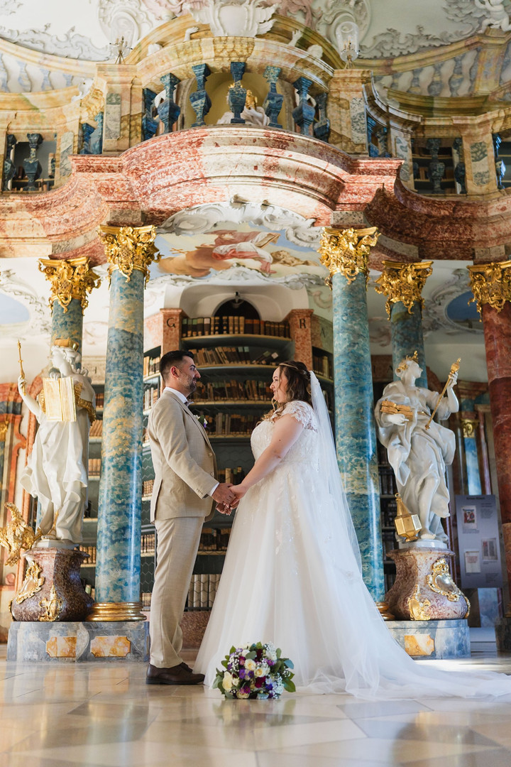 Hochzeit Kloster Wiblingen: Brautpaar hält sich an den Händen zwischen den Säulen im Bibliothekssaal