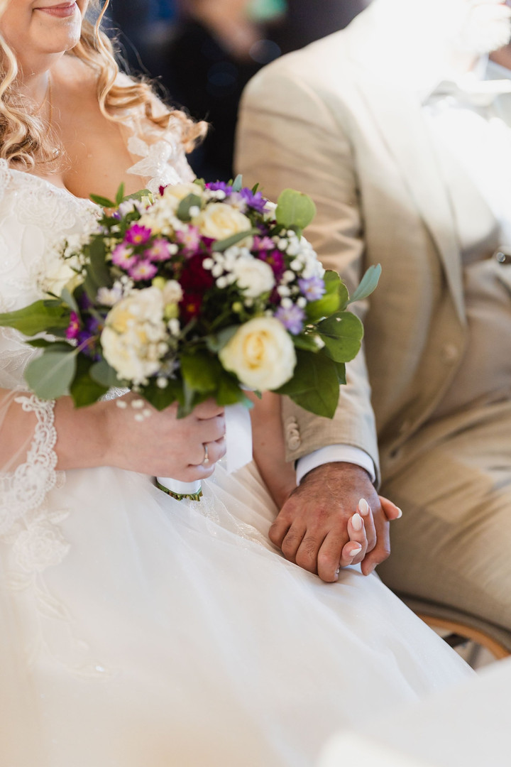 Hochzeit Kloster Wiblingen: Brautpaar hält sich bei der Trauung an den Händen, Brautstrauß im Vordergrund