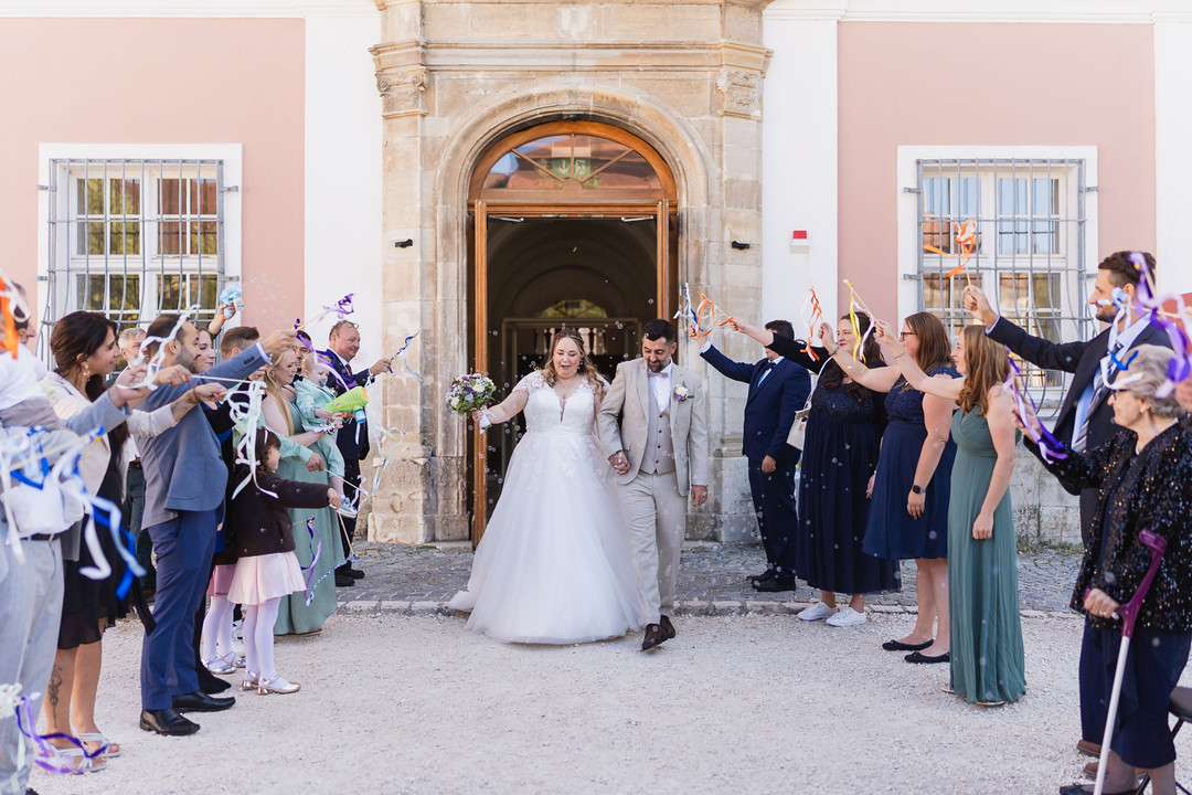 Hochzeit Kloster Wiblingen: Brautpaar tritt beim Spalier mit Seifenblasen und Bändchen aus dem Portal