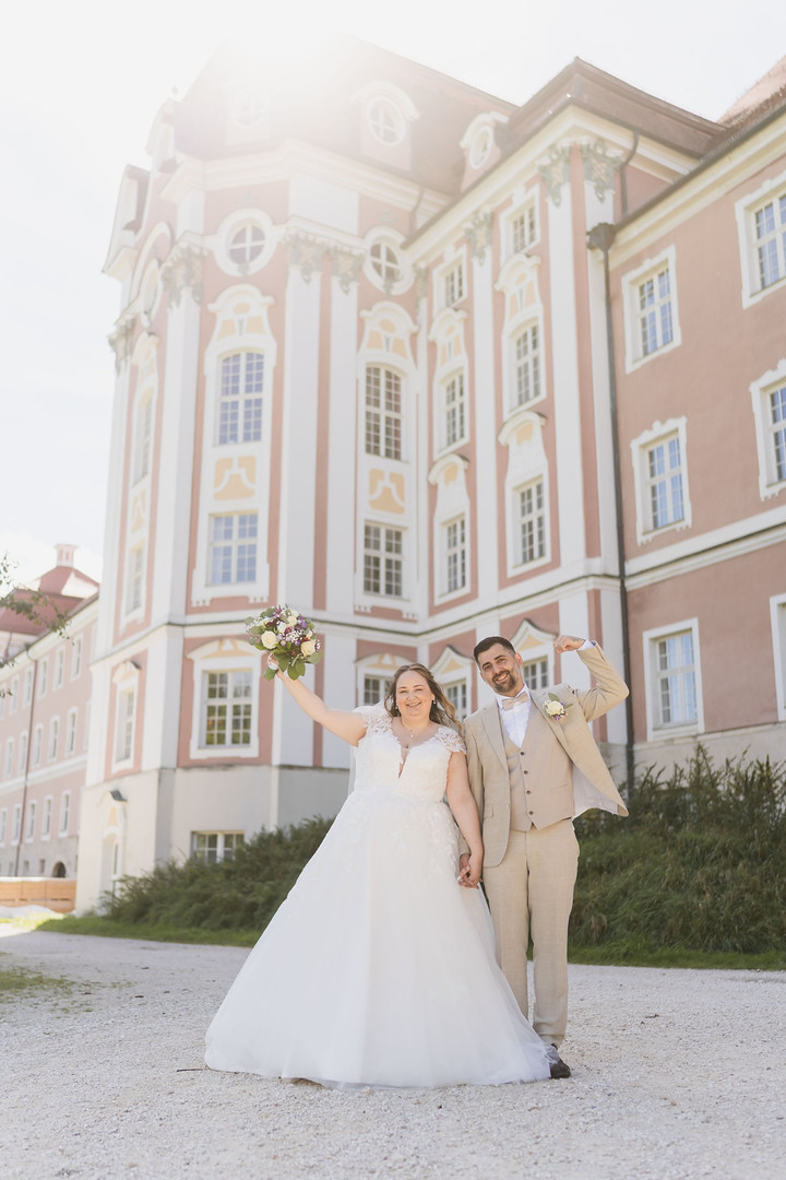 Hochzeit Kloster Wiblingen: Brautpaar jubelt vor der Klosterfassade, Braut mit Brautstrauß in der Hand